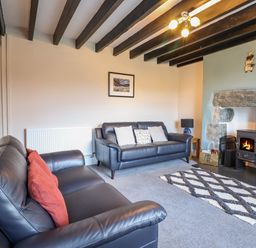 A living room with two leather sofas a wood burning stove and a patterned rug at Ynys in Dyffryn Ardudwy