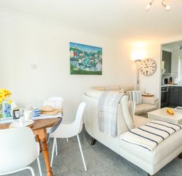 A living area with white sofa and wooden dining table with chairs near a kitchen at Gull Cottage in Kessingland