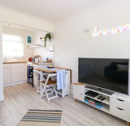 A small kitchen and living area with a TV on a stand and a dining table with chairs at Dollys Lookout in Kessingland