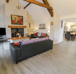 An open living room and dining area with sofas a coffee table a fireplace a television and a dining table with chairs at Bodrual Cottage in Rhosbodrual near Caernarfon