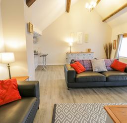 A living room with two black sofas with red and patterned cushions a wooden sideboard and bar stools at Bodrual Cottage in Rhosbodrual near Caernarfon