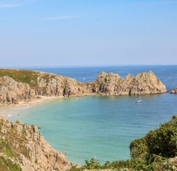 A rocky coastline with a sandy beach and a boat on the water at Beachcomber in Porthcurno near Sennen