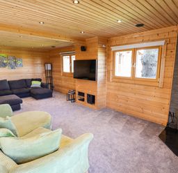 A living room with wood panel walls a green chair a dark sectional sofa a wall-mounted TV and a fireplace at iLodge Ultra Kenwick near Louth