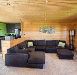 A living room with a large dark sectional sofa and a floor lamp beside wooden walls at iLodge Ultra Kenwick near Louth