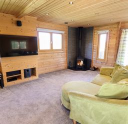 A living room with wooden walls a green sofa a fireplace and a wall mounted television at iLodge Ultra Kenwick near Louth