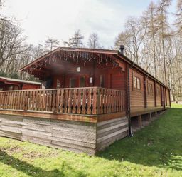 A wooden cabin with a covered porch surrounded by grass and trees at iLodge 73 Kenwick near Louth