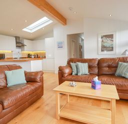 A living room with two brown leather sofas a wooden coffee table and an open kitchen at 10 Faraway Fields in Dobwalls