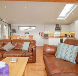 A living room with two brown leather sofas a wooden coffee table wooden dining table and chairs and a kitchen area at 10 Faraway Fields in Dobwalls
