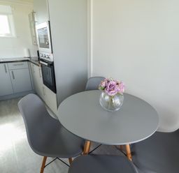 A kitchen with gray cabinets a gray round table with pink flowers in a vase and gray chairs at 23 Cherry Park in Chapel St Leonards