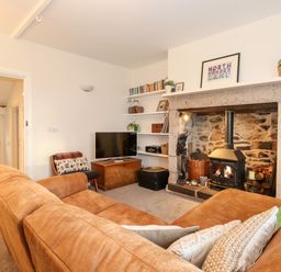 A living room with a brown sofa a stone fireplace with a wood stove a TV and shelves with books at Garden Cottage in Chathill near Beadnell
