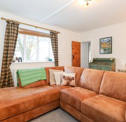 A living room with a brown leather corner sofa green throw and plaid curtains at Garden Cottage in Chathill near Beadnell