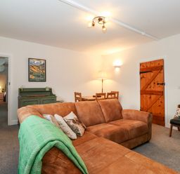A living room with a brown sofa green cabinet wooden dining table and wooden door at Garden Cottage in Chathill near Beadnell