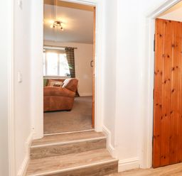 A hallway with wooden doors and steps leading to a room with a brown sofa at Garden Cottage in Chathill near Beadnell