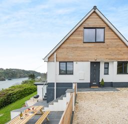 A house with wooden paneling and gravel driveway near a coastline with trees and water at Beach View in Combe Martin