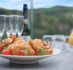 A plate with croissants, pastries, and strawberries on a table with glasses, a bottle, and a jug of orange juice in the background at Beach View in Combe Martin