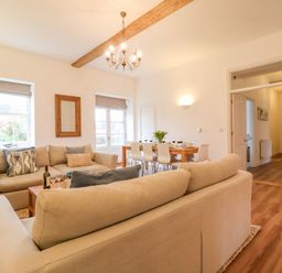 A living room with two beige sofas a wooden dining table with white chairs and a chandelier at Feathers Blythburgh in Reydon