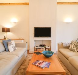 A living room with two sofas a wooden coffee table and a wall-mounted television at Feathers Blythburgh in Reydon