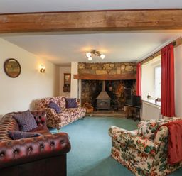 A living room with floral and leather sofas a stone fireplace and a wood stove at Canny Croft in Chilton Polden near Street