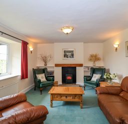 A living room with two brown leather sofas two green armchairs a wooden coffee table and a fireplace at Canny Croft in Chilton Polden near Street