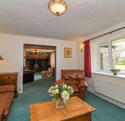 A living room with brown leather sofas wooden coffee table and a window with red curtains at Canny Croft in Chilton Polden near Street