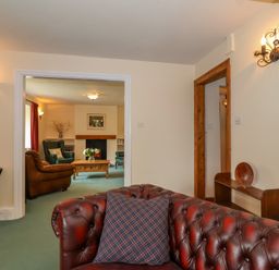 A room with a brown leather sofa and a blue plaid pillow looking into another room with green and brown armchairs a wooden coffee table and a fireplace at Canny Croft in Chilton Polden near Street