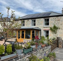 A stone house with solar panels on the roof and potted plants in front at Woodbine Cottage in Mylor Bridge Nr Falmouth