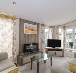 A living room with sofas glass coffee table television and floral curtains at Gwydn Lodge in Downton Hampshire