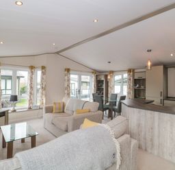 An open living area with two sofas a glass coffee table a television dining table and a kitchen with cabinets at Gwydn Lodge in Downton Hampshire