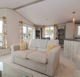 A living room with a beige sofa yellow cushions and floral curtains at Gwydn Lodge in Downton Hampshire
