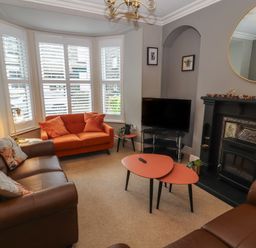 A living room with brown and orange sofas a black fireplace and a television at Snowflake Cottage in Windermere