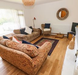A living room with two sofas a wicker chair a rug and a TV on a stand at Glynderi in Cilgerran