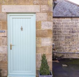 A blue front door with a brass handle and a knocker on a stone wall with two potted plants at The Byre in Longwitton near Morpeth