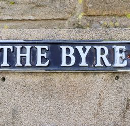 A metal sign with the words THE BYRE on a stone wall at The Byre in Longwitton near Morpeth