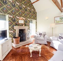 A living room with a fireplace a television and patterned wallpaper at The Byre in Longwitton near Morpeth