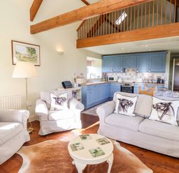 A living room with armchairs and sofa near a round coffee table and a kitchen with blue cabinets at The Byre Longwitton near Morpeth