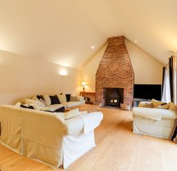 A living room with sofas around a wooden coffee table and a brick fireplace at The Stables at Hall Barn in Wattisfield near Walsham-Le-Willows