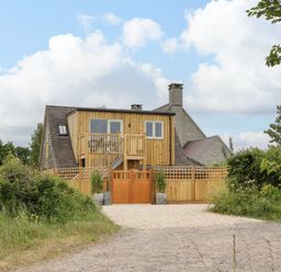 A wooden fenced house with a balcony and stairs surrounded by greenery and a gravel driveway at The Attic at Redmond Bottom in Wookey