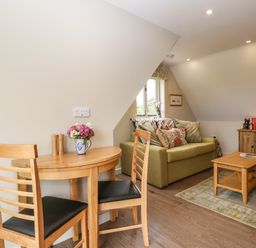 A small dining table with two chairs a green sofa with cushions a wooden coffee table and a wooden desk with a lamp at The Attic at Redmond Bottom in Wookey