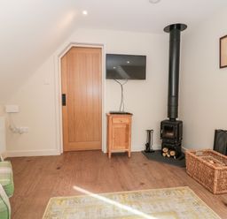 A sitting area with a green plaid armchair a wooden door a wall-mounted TV a wood-burning stove and a wicker basket at The Attic at Redmond Bottom in Wookey