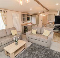 A living room with beige sofas and yellow pillows a wooden coffee table with flowers and an open kitchen with dining area at 20 Wolds View East Heslerton near West Heslerton