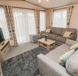 A living room with two sofas a coffee table a TV on a wooden stand a gray rug and curtains at 20 Wolds View East Heslerton near West Heslerton