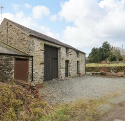 A stone barn with large wooden doors and a gravel driveway surrounded by trees at Myra's View in Newby Bridge