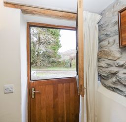 A wooden stable door partially open with curtains and a stone wall inside a house at Myra's View in Newby Bridge