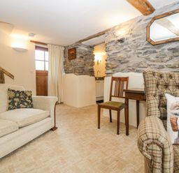 A sitting room with a beige sofa a wooden chair a plaid armchair with a sheep cushion stone walls and a wooden door at Myra's View in Newby Bridge