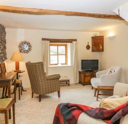 A sitting room with chairs a wooden table a television and a window at Myra's View in Newby Bridge