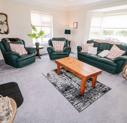 A living room with green leather sofa and armchairs with striped cushions a wooden coffee table on a rug and windows with blinds at The Glen in Carndonagh County Donegal