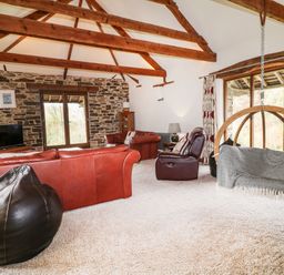 A living room with leather sofas a hanging chair and exposed wooden beams at Birchenhayes in St Dominick