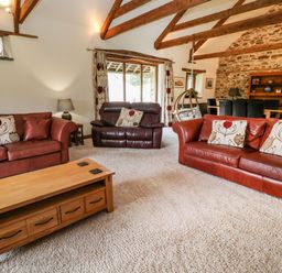 A living room with leather sofas wooden coffee table and exposed wooden beams at Birchenhayes in St Dominick