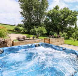 An outdoor hot tub with bubbling water in a garden with trees and greenery at Birchenhayes in St Dominick