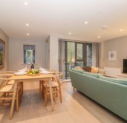 A dining table with six chairs set with bowls and glasses next to a living area with a green sofa and a television at Bruach in Backbarrow